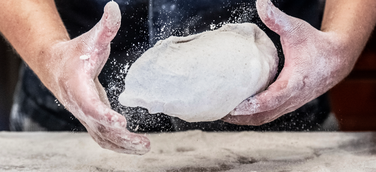 Närbild på en bagares händer, som kastar en deg.