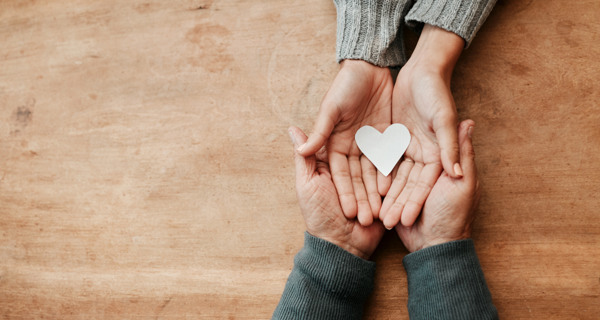 Bild på två par händer med handflatorna uppåt som håller i ett hjärta av papper.