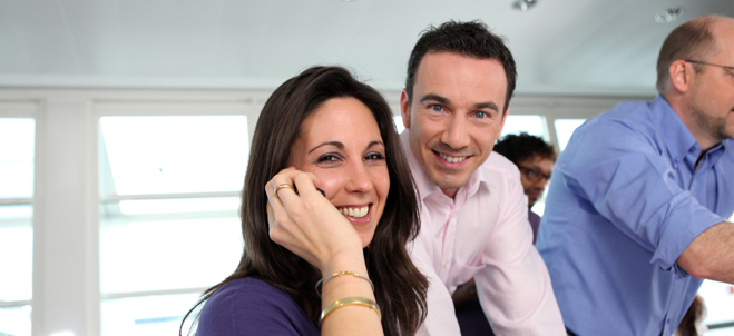 Två kollegor på en arbetsplats ler in i kameran