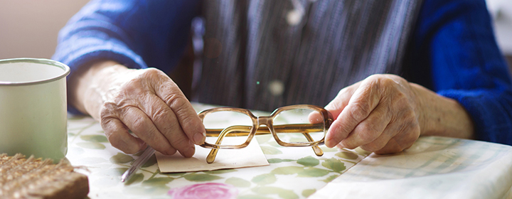 En äldre kvinnas händer håller i glasögon vid ett bord