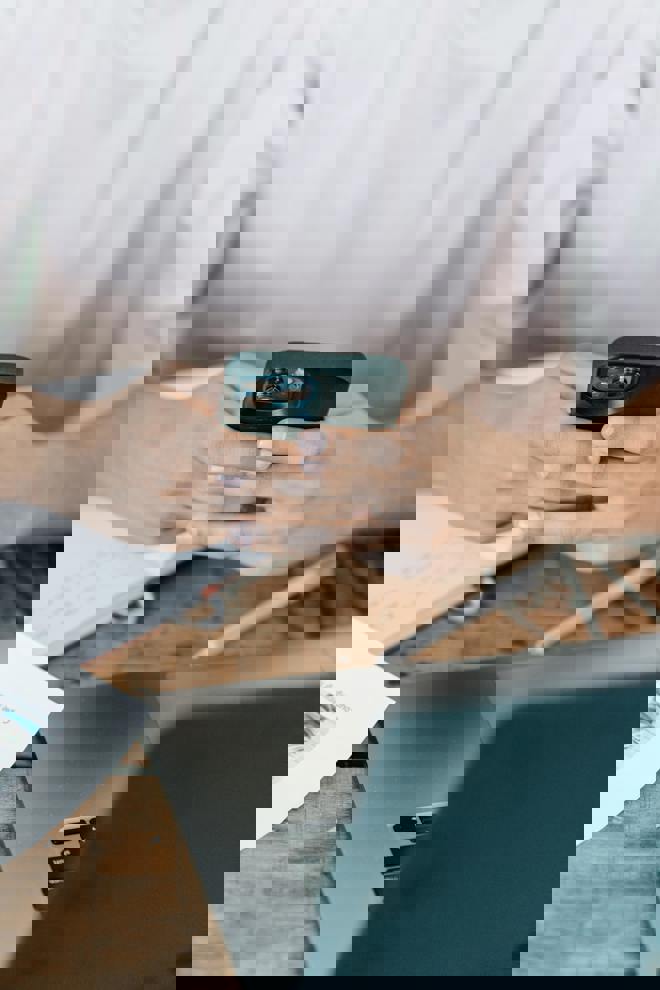 Bild på händer som håller i en telefon, framför en dator