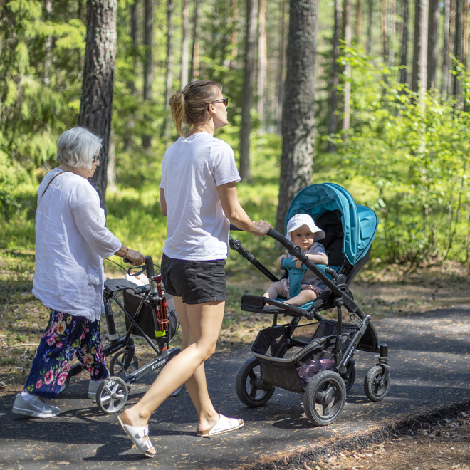 Bild som visar två personer på en gångväg i skogen, en med barnvagn och en med rullator.
