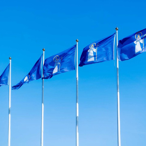 Bild på ett antal Södertälje kommun-flaggor som vajar i vinden mot en blå himmel.