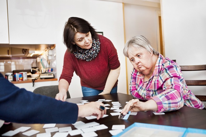 personal hjälper kvinna med funktionsnedsättning med kort på ett bord